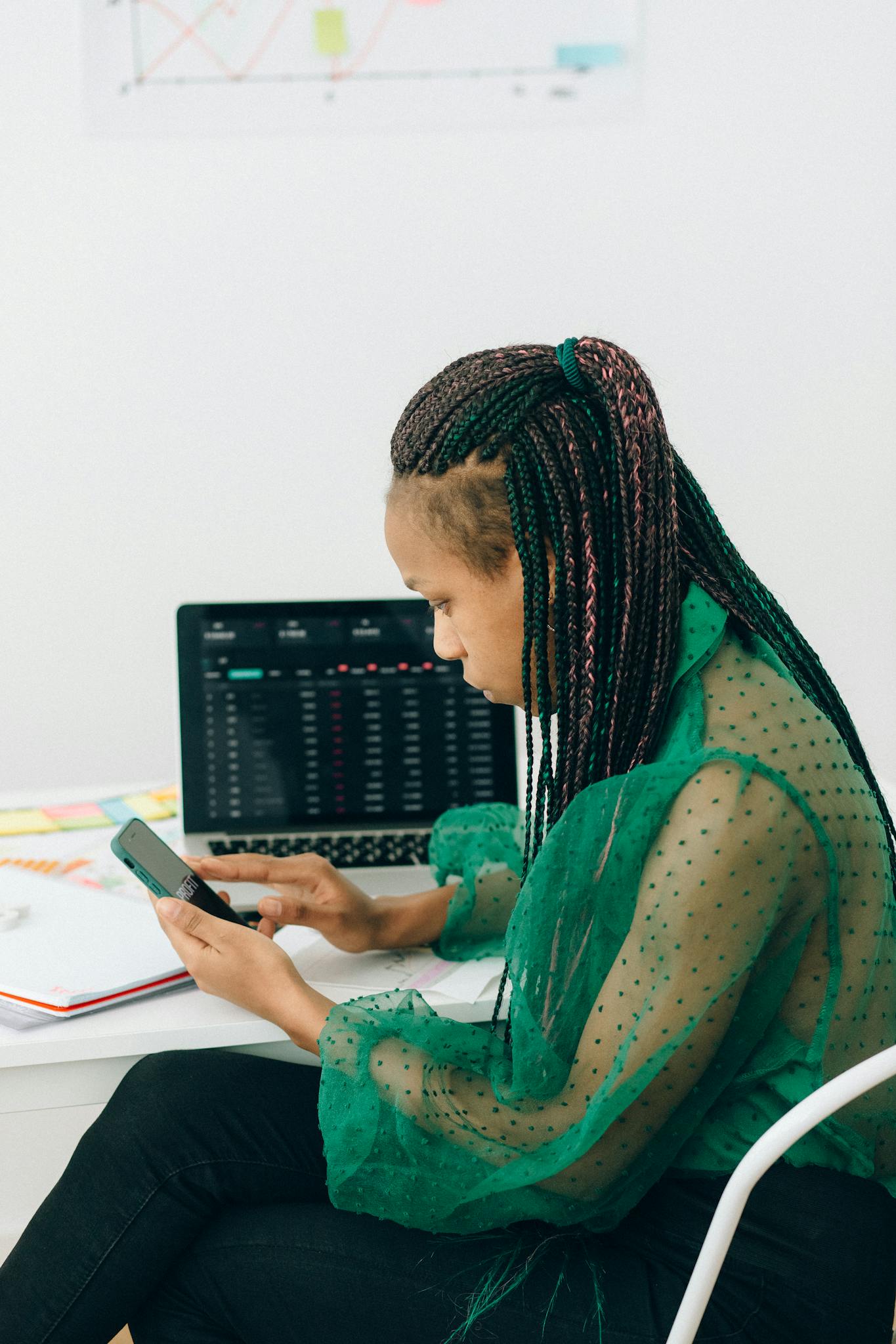 Businesswoman analyzing stock market data using smartphone and laptop indoors.